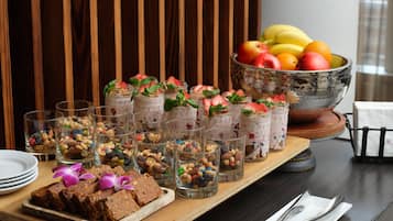A buffet table with various food items, including jars of dessert, a bowl of fruit, and a tray of brownies.