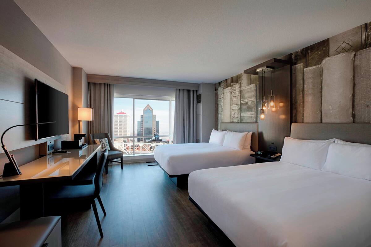Ein Hotelzimmer mit zwei Betten, einem Schreibtisch, einem Fernseher und Blick auf die Stadt.