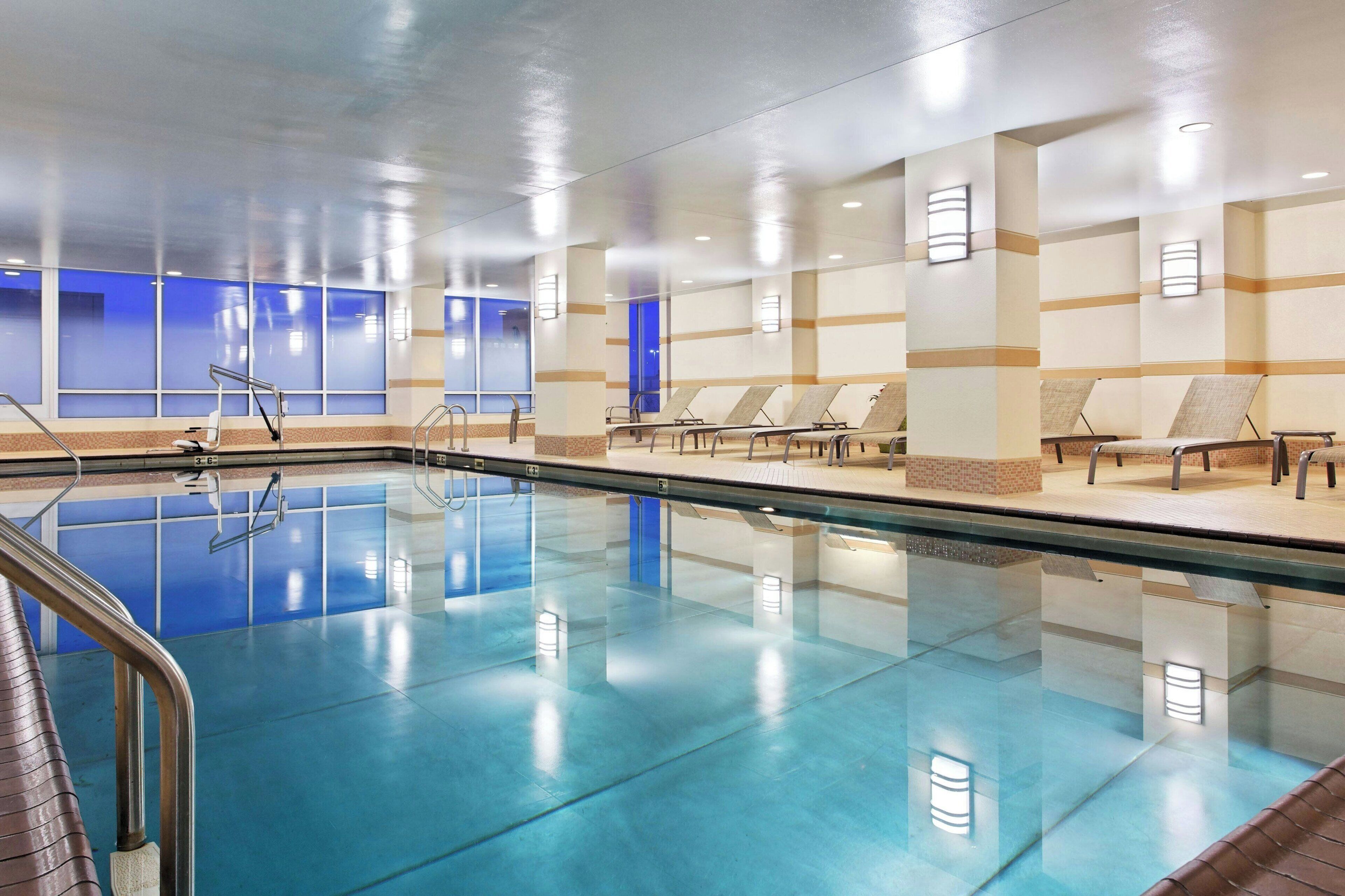A large indoor swimming pool with clear blue water, surrounded by lounge chairs and a tiled floor.