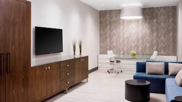 A modern living room with a large TV, a blue sofa, a glass coffee table, and a herringbone-patterned wall.