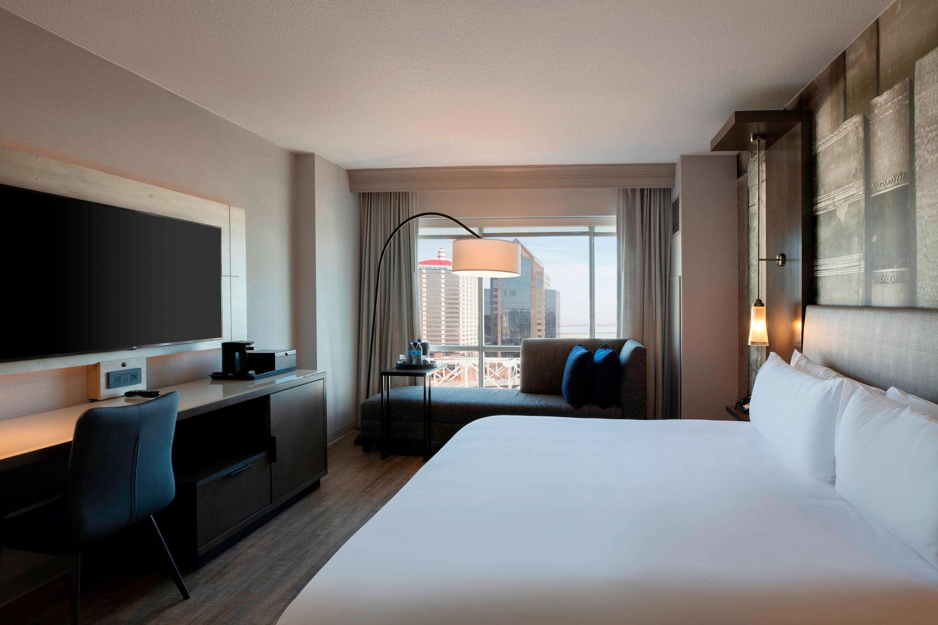 Una habitación de hotel con una cama grande, un escritorio con televisor de pantalla plana, un sofá y una ventana con vistas a la ciudad.