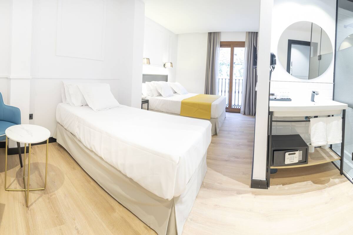 Habitación de hotel con dos camas, un escritorio, una silla, un baño con espejo y vistas al exterior.