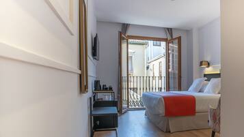 A hotel room with a bed, a desk, a chair, a TV, and a balcony with a railing.