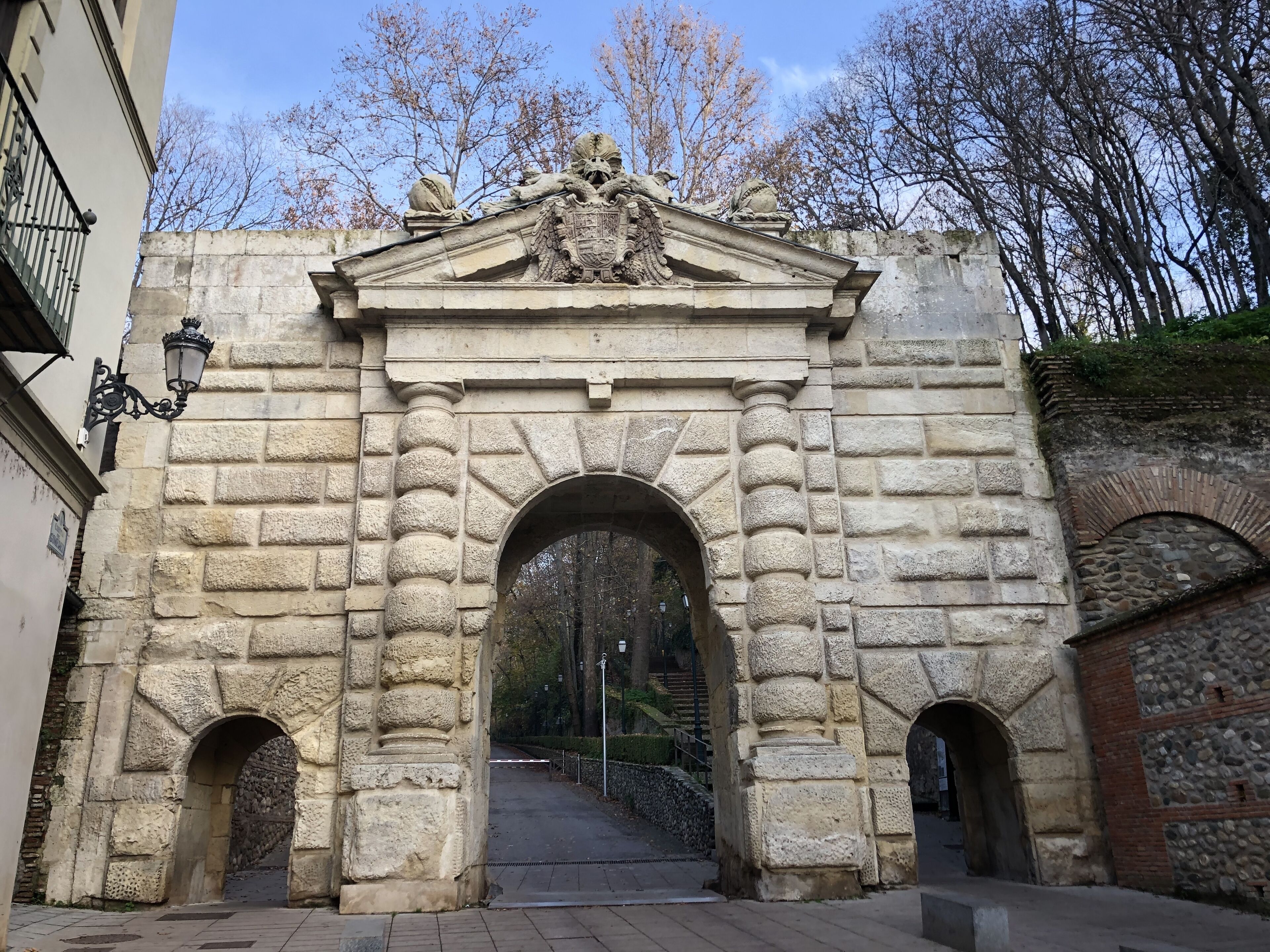 Un arco de piedra con un escudo de armas, flanqueado por dos arcos más pequeños y un farol a la izquierda.