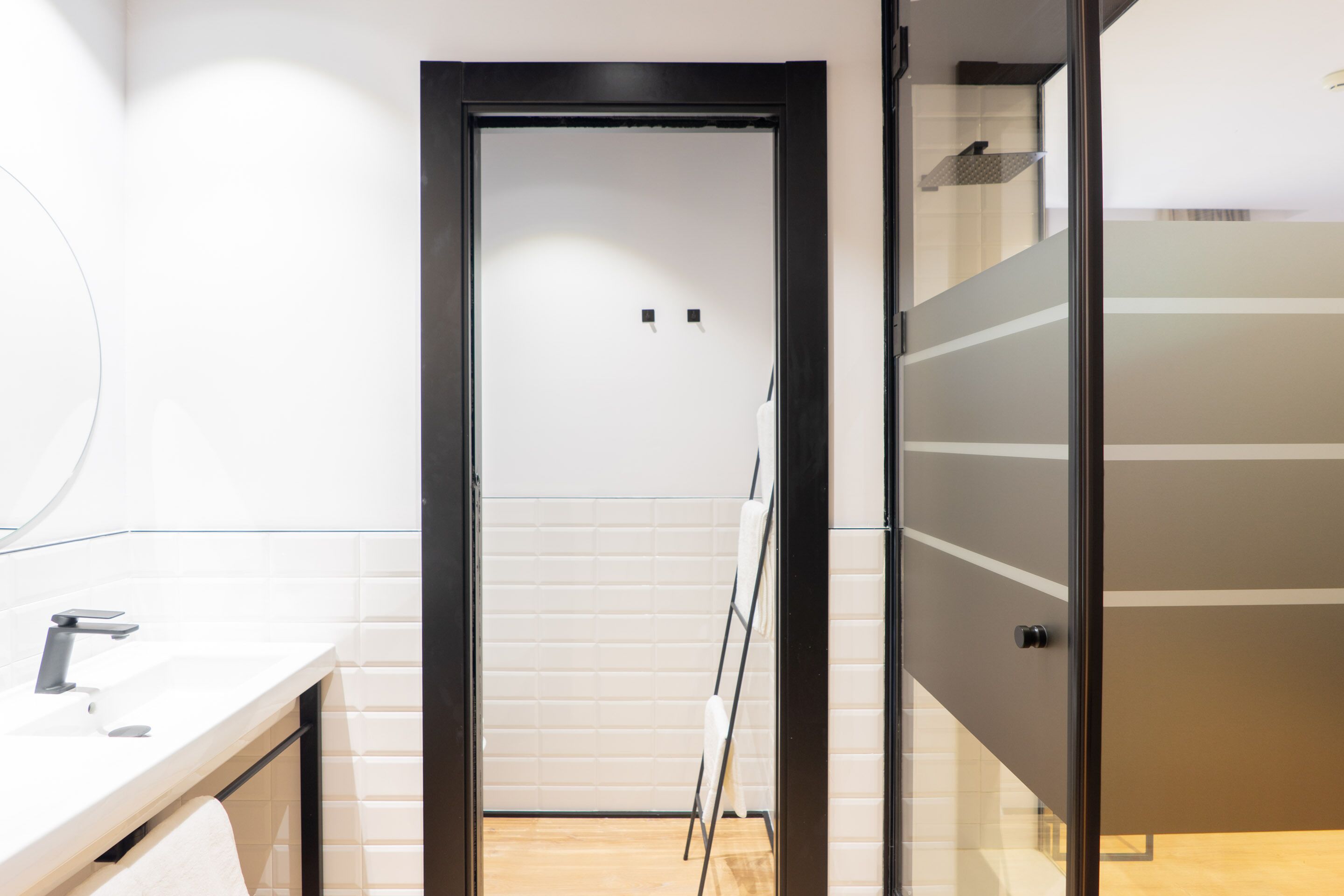 Un baño moderno con un lavamanos blanco, un espejo y una puerta de vidrio que da a la zona de la ducha.