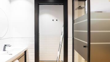Un baño moderno con un lavamanos blanco, un espejo y una puerta de vidrio que da a la zona de la ducha.
