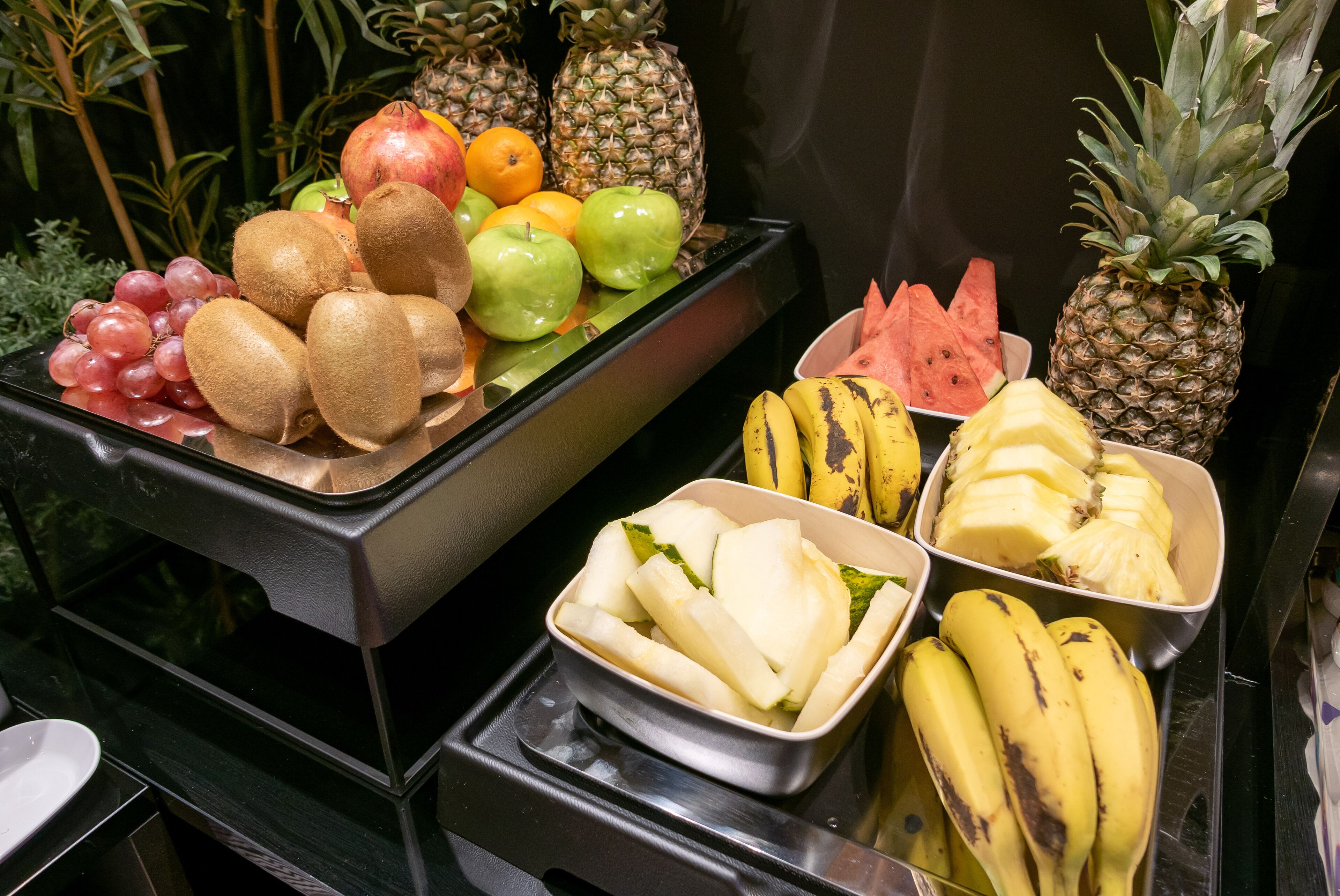 Una exhibición de frutas con diversas opciones como uvas, kiwis, manzanas y plátanos.