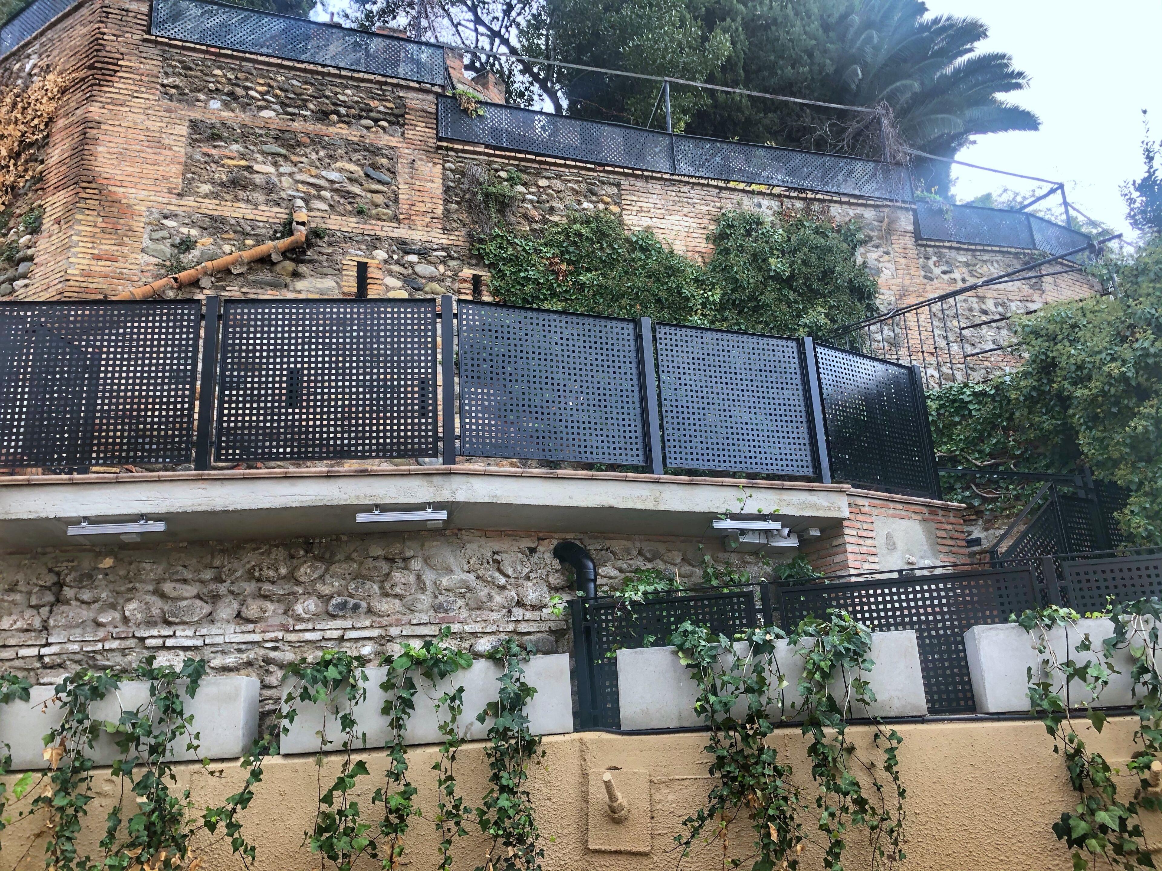 Un edificio de piedra con un balcón, barandilla de malla metálica y hiedra cubriendo las paredes.