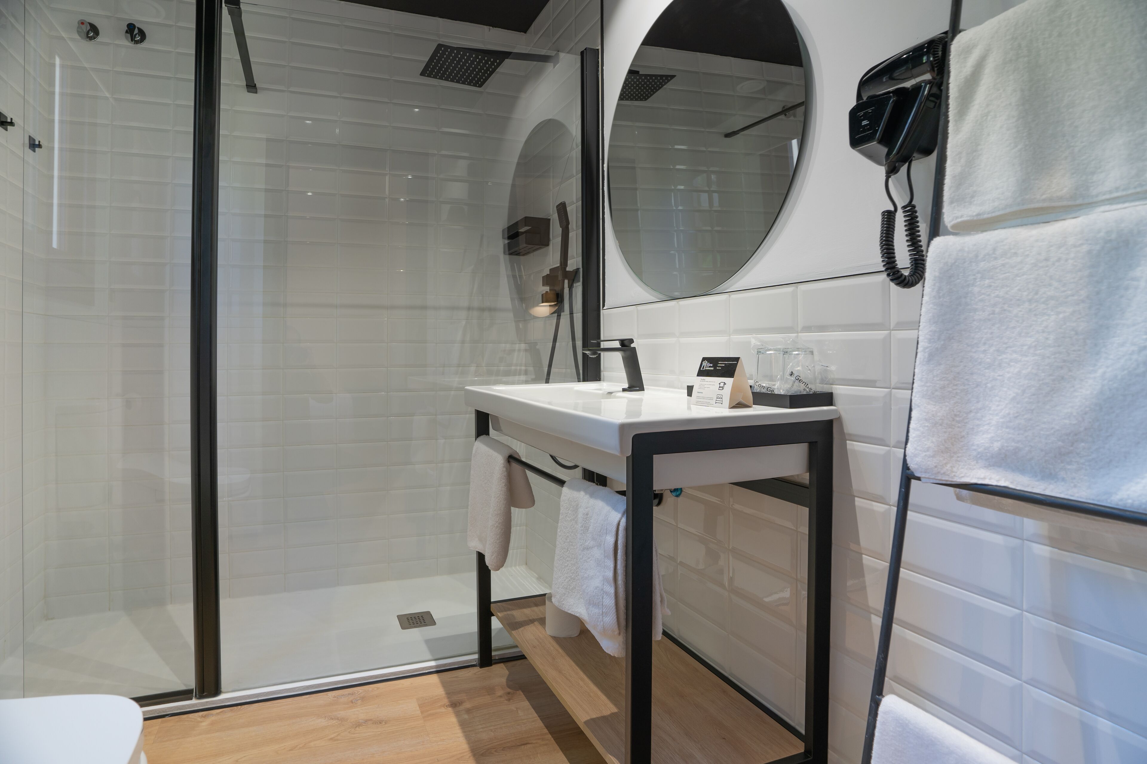 Un baño moderno con cabina de ducha de vidrio, un lavamanos blanco con espejo y un teléfono fijado a la pared.
