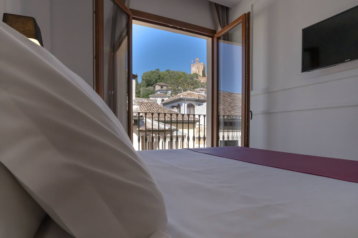 Un dormitorio con cama, vistas a un pueblo con edificios y una torre, y un televisor montado en la pared.