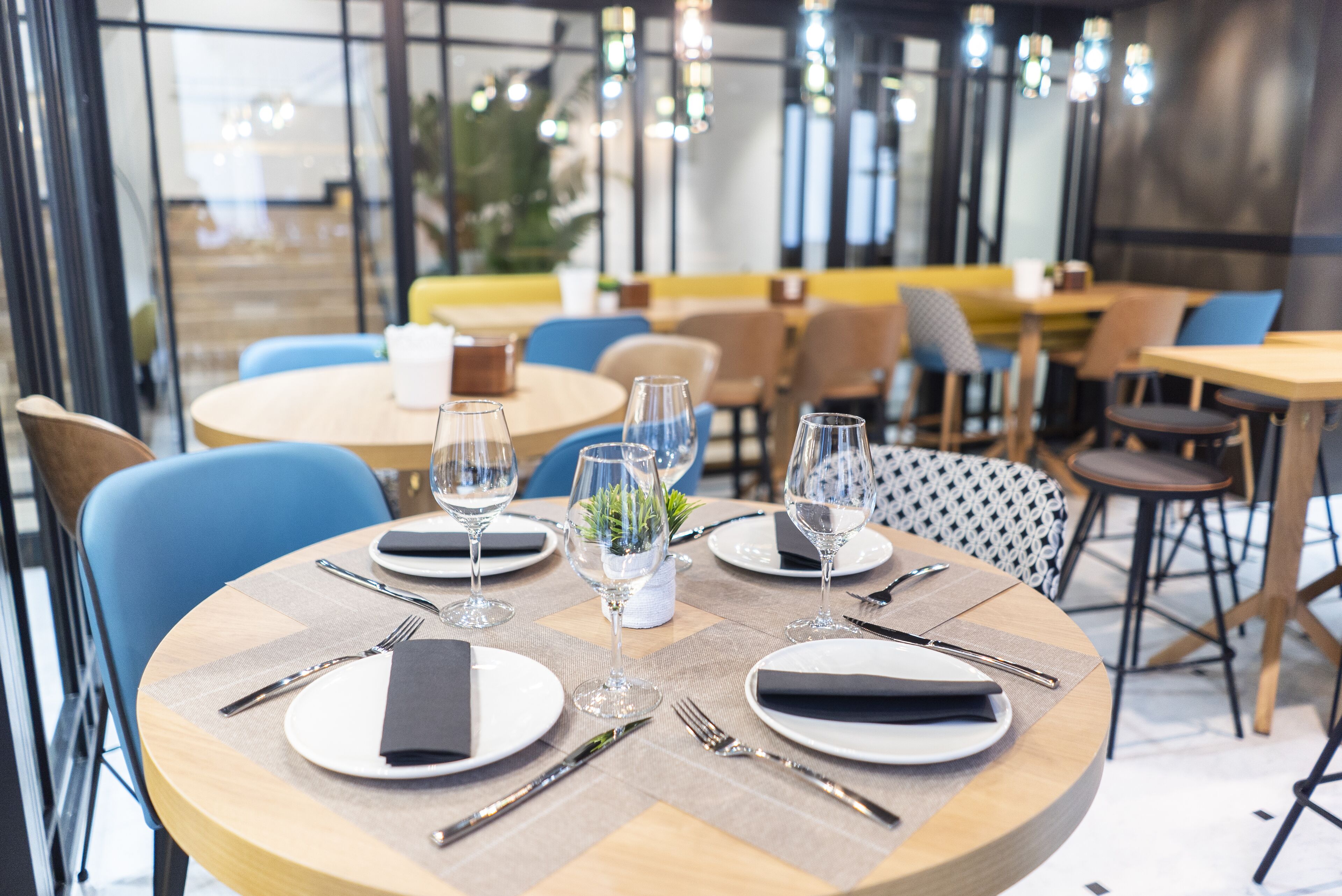 A dining area with round tables set for four, each with plates, cutlery, and napkins.
