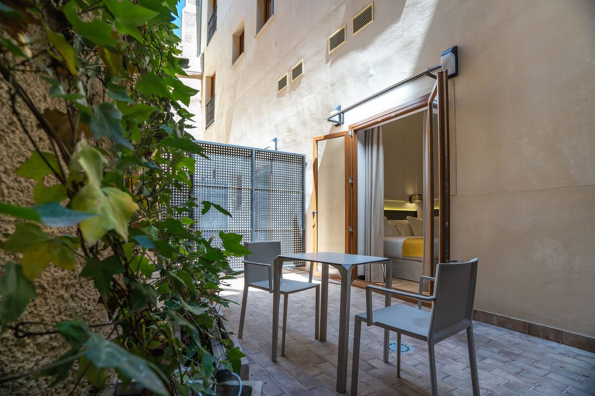 An outdoor patio area with a table and chairs, a wooden door, and a wall with a window.