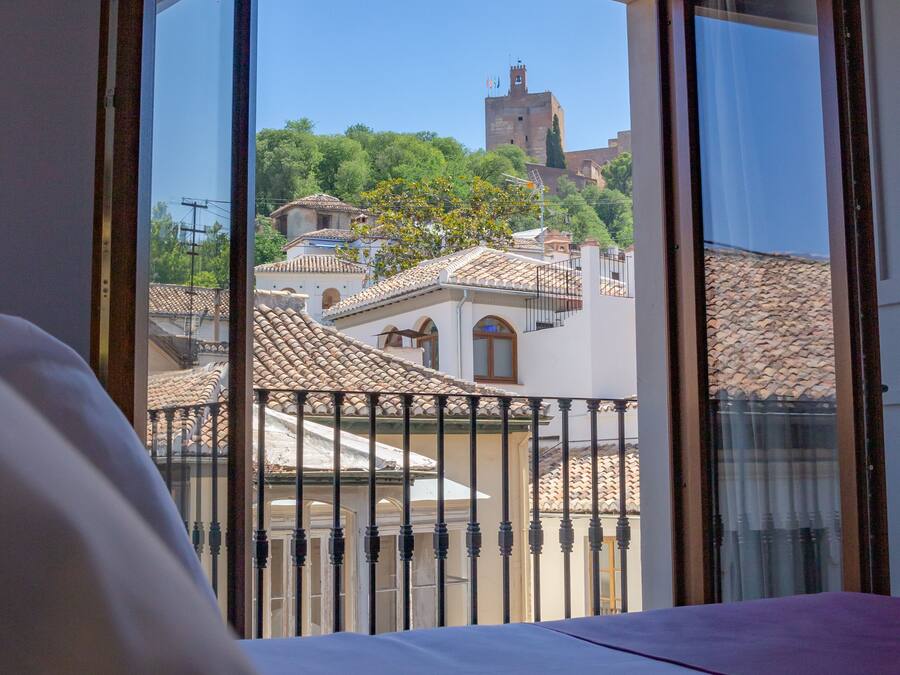Habitación de hotel con balcón que da a un paisaje urbano con edificios históricos y una iglesia.