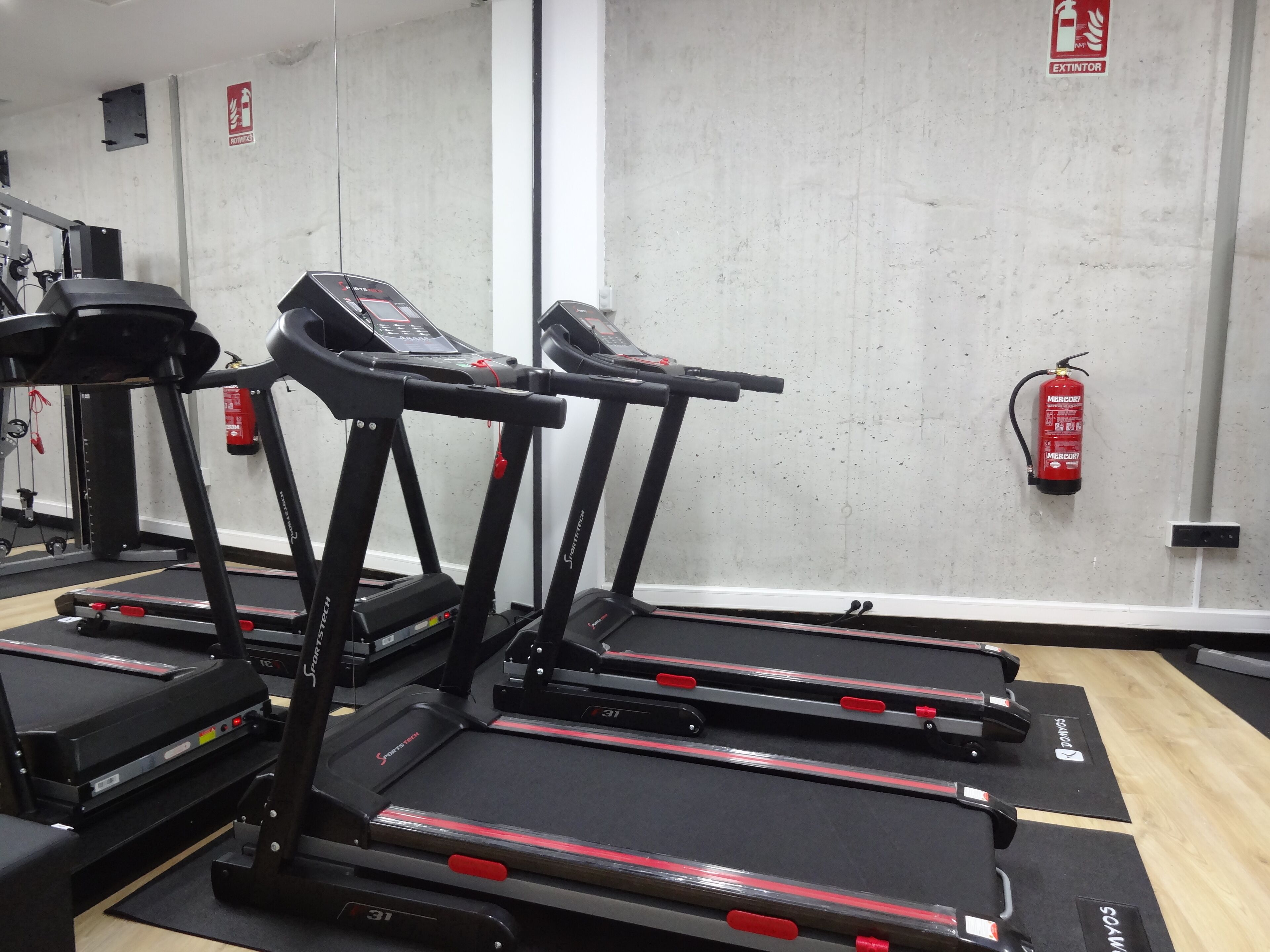 A gym with treadmills, exercise equipment, and a fire extinguisher on the wall.