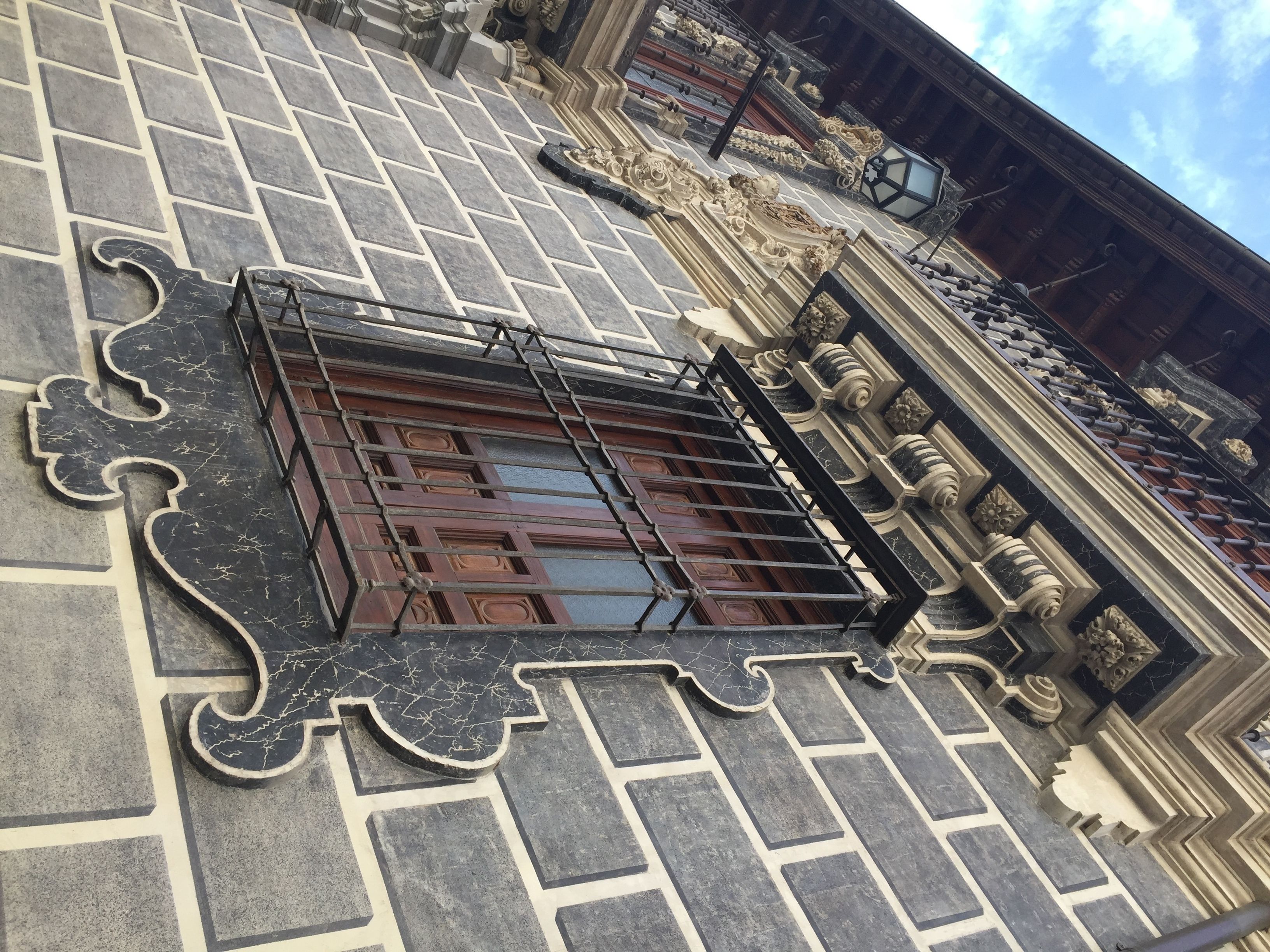 Fachada de edificio con suelo de piedra estampada, ventana decorativa con celosía metálica y detalles arquitectónicos ornamentales.
