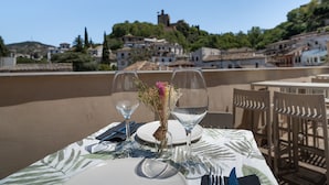 Mesa dispuesta para dos con copas de vino y un florero, con vistas a un pueblo en la ladera.