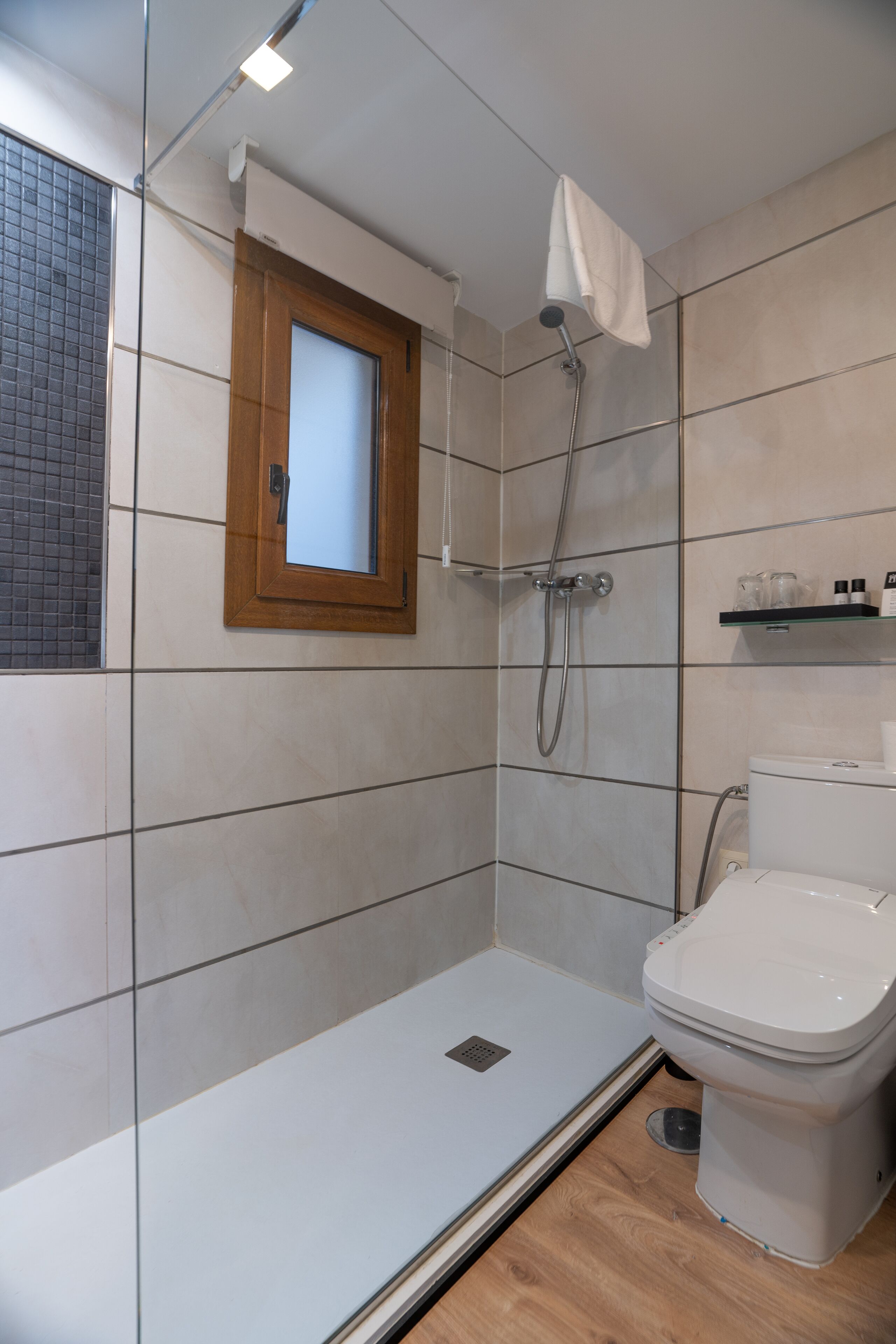 A modern bathroom with a glass shower enclosure, a toilet, and a small window.