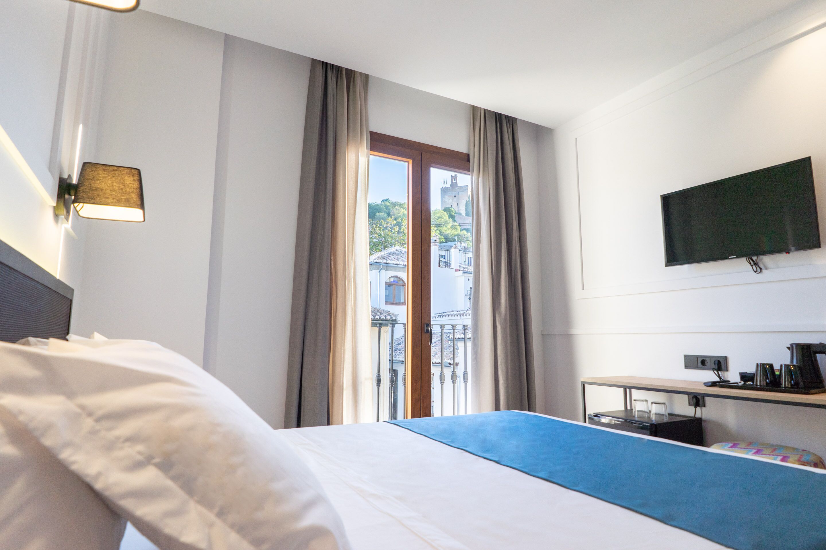 A hotel room with a bed, a desk with a computer, a flat-screen TV, and a window with curtains.