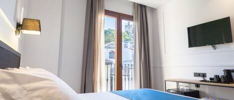 A hotel room with a bed, a desk with a computer, a flat-screen TV, and a window with curtains.
