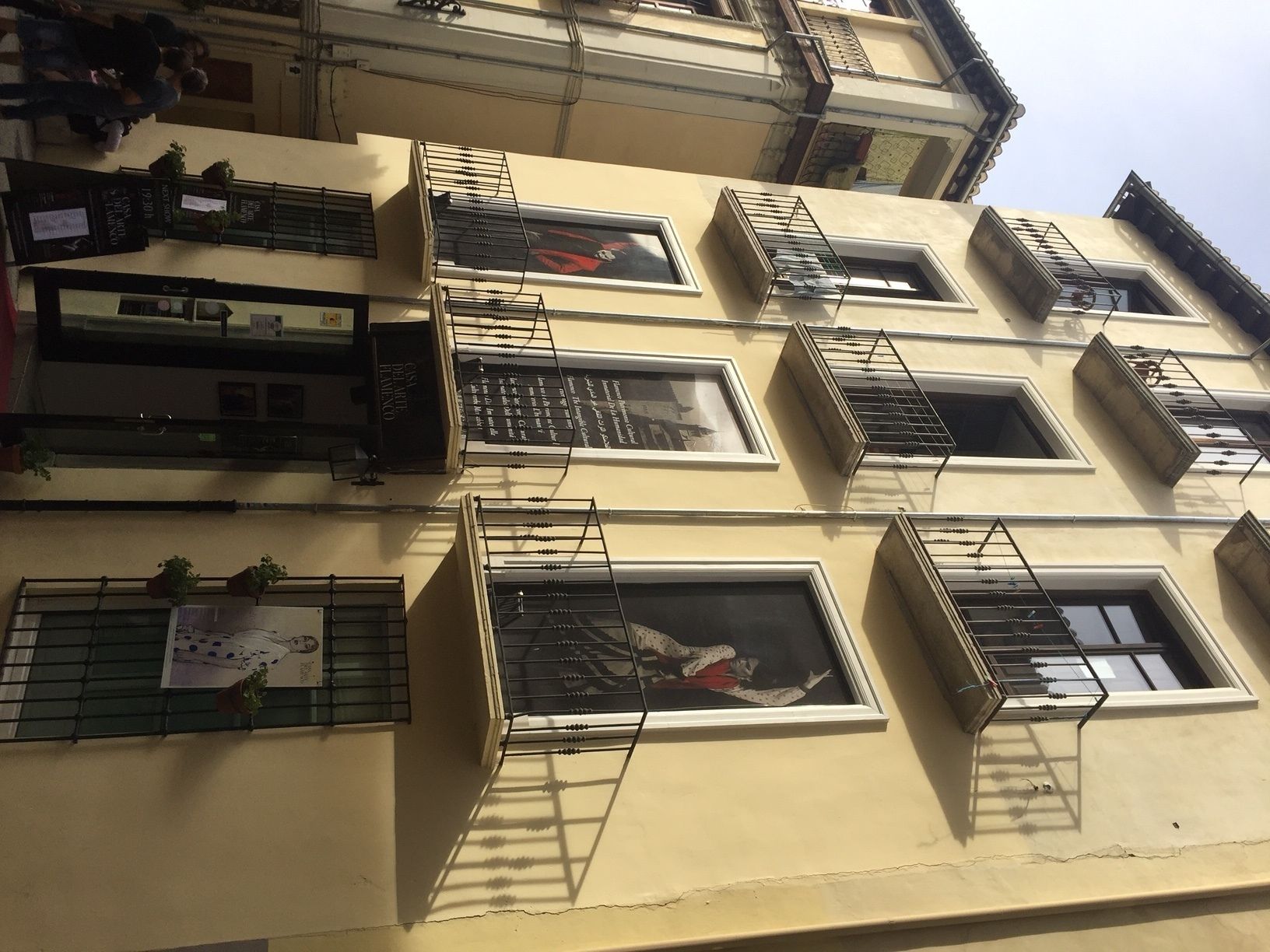 Un edificio de varios pisos con balcones, ventanas y algunas macetas con plantas.