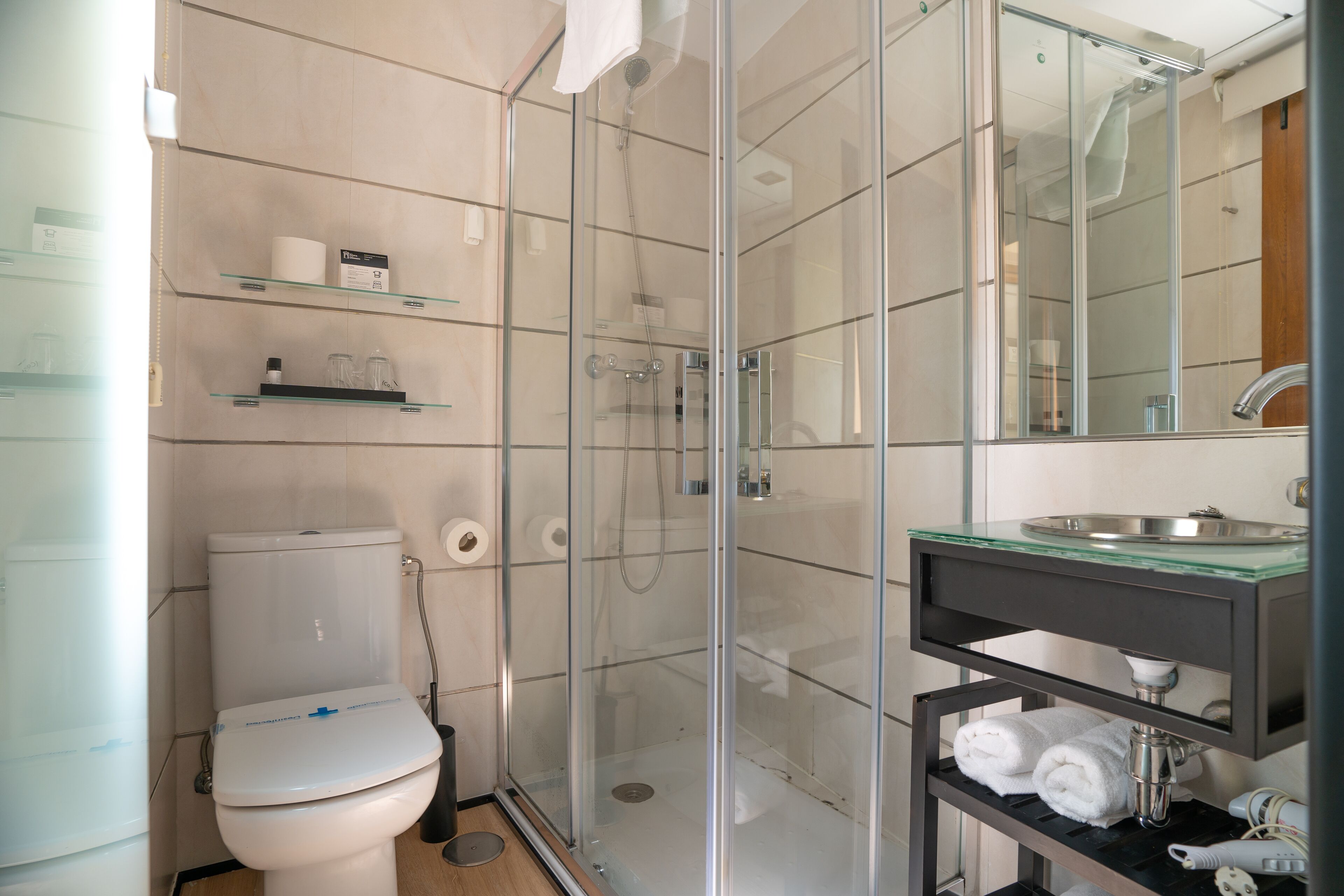 A modern bathroom with a glass-enclosed shower, a toilet, and a sink with a glass countertop.