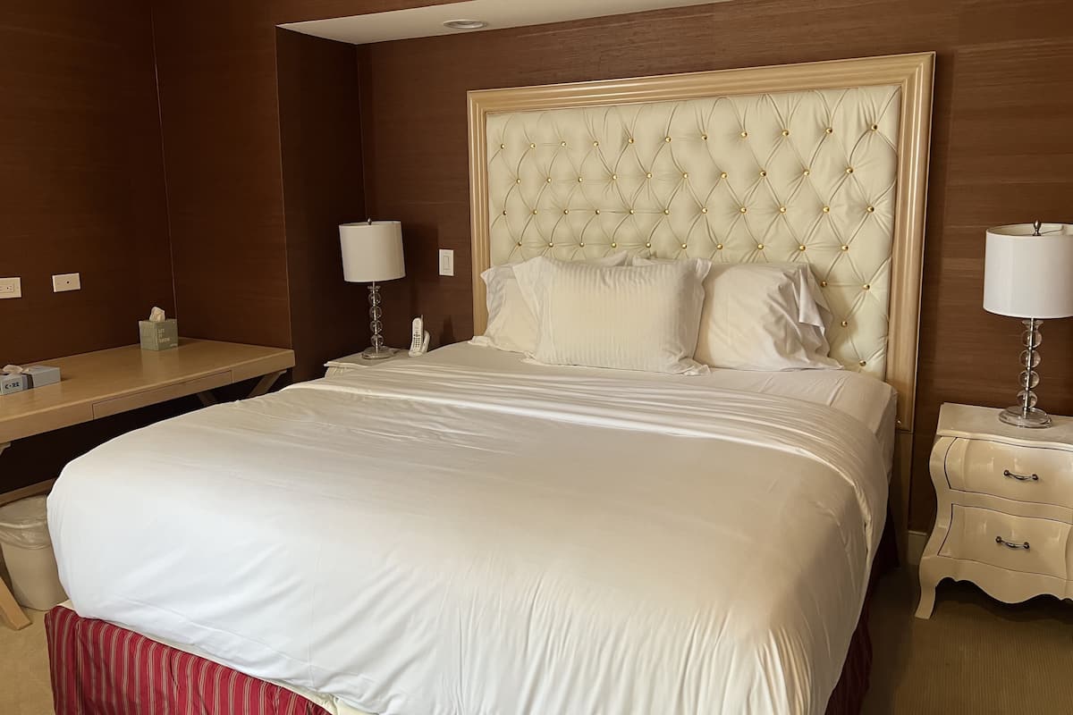 A hotel room with a large bed, two bedside tables, a nightstand, a mirror, and a wall-mounted telephone.
