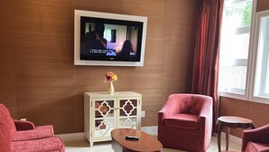 Ett modernt vardagsrum med en tv som hänger på väggen, ett litet skåp med en vas med blommor och två röda fåtöljer.