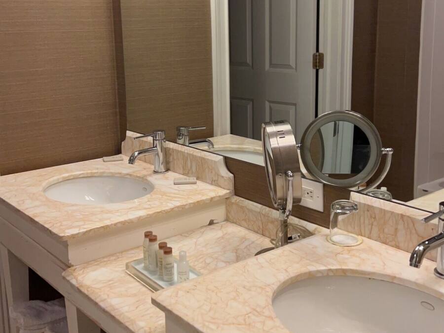 Un baño con tres lavamanos, un espejo grande y una puerta que da a otra habitación.