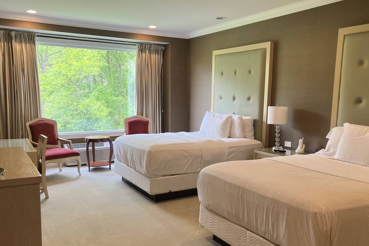 A hotel room with two beds, a desk, a chair, and a window with curtains.