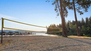 Cancha de voleibol de playa con red, rodeada de árboles y vista al agua.