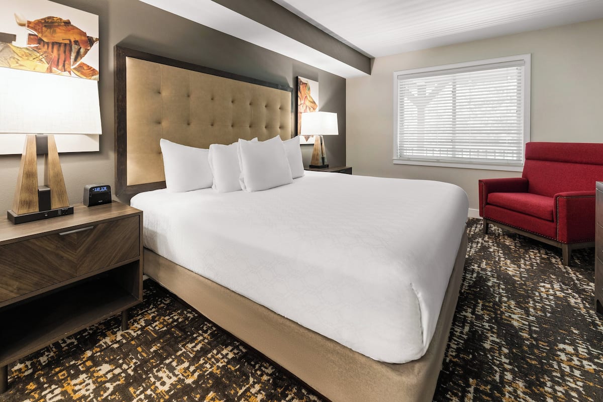 A hotel room with a large bed, a red armchair, and a nightstand with a lamp.