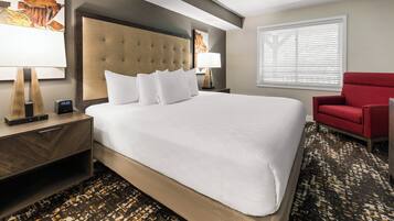 A hotel room with a large bed, a red armchair, and a nightstand with a lamp.