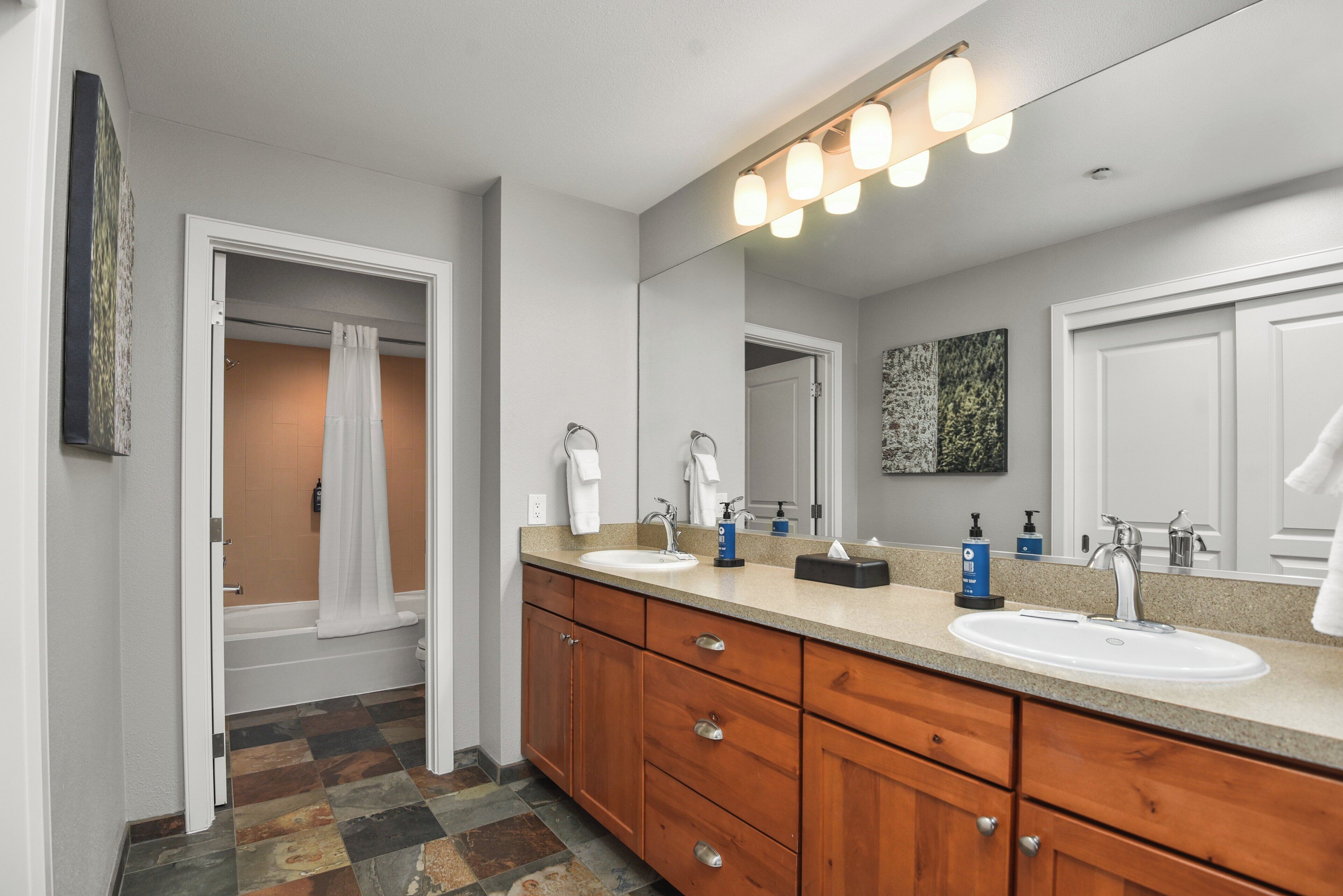 A bathroom with a double sink vanity, a large mirror, and a shower area.