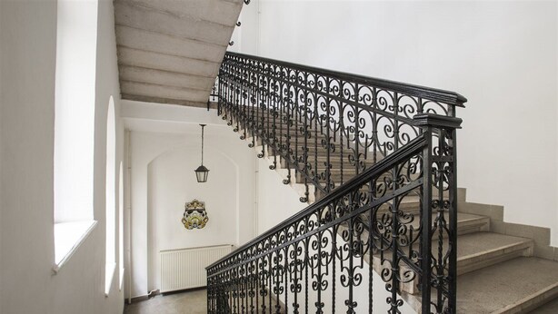 Una escalera con barandillas de metal negro ornamentadas y peldaños color beige.