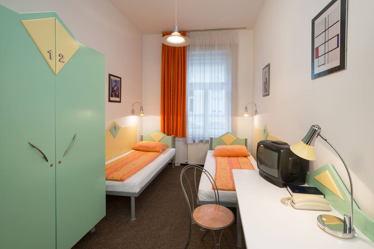 A compact room with two single beds, a desk with a television, and a chair.