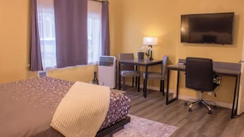 A hotel room with a bed, desk, chair, television, and a window with curtains.