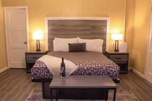 A hotel room with a large bed, bedside tables, a nightstand, a desk, and a chair. - Carmel Wayfarer Inn (Carmel)