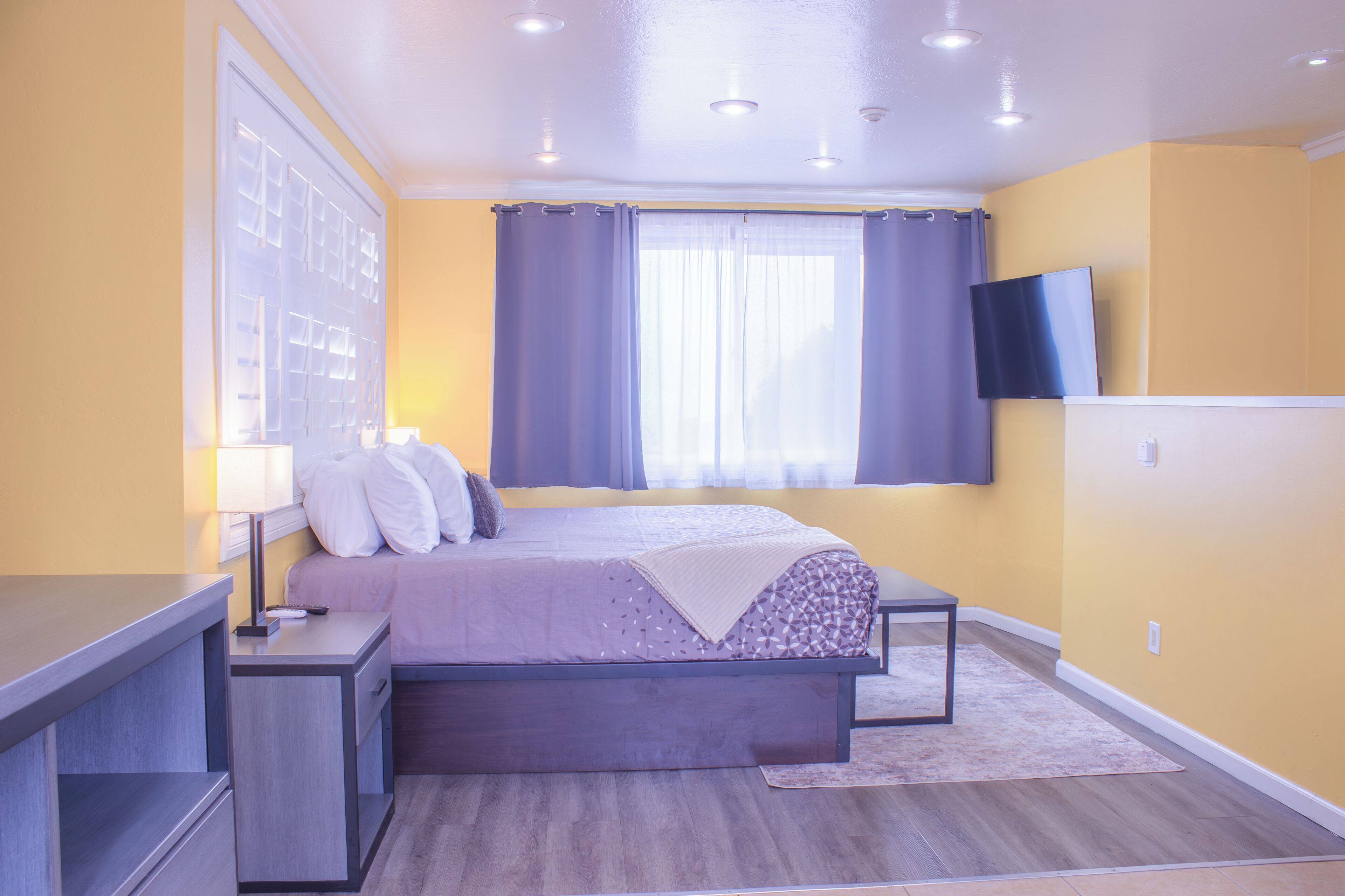 A bedroom with a bed, bedside tables, a TV, and a window with curtains.