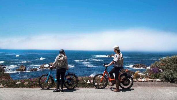 Deux personnes à vélo, sur une route côtière offrant une vue sur l’océan.