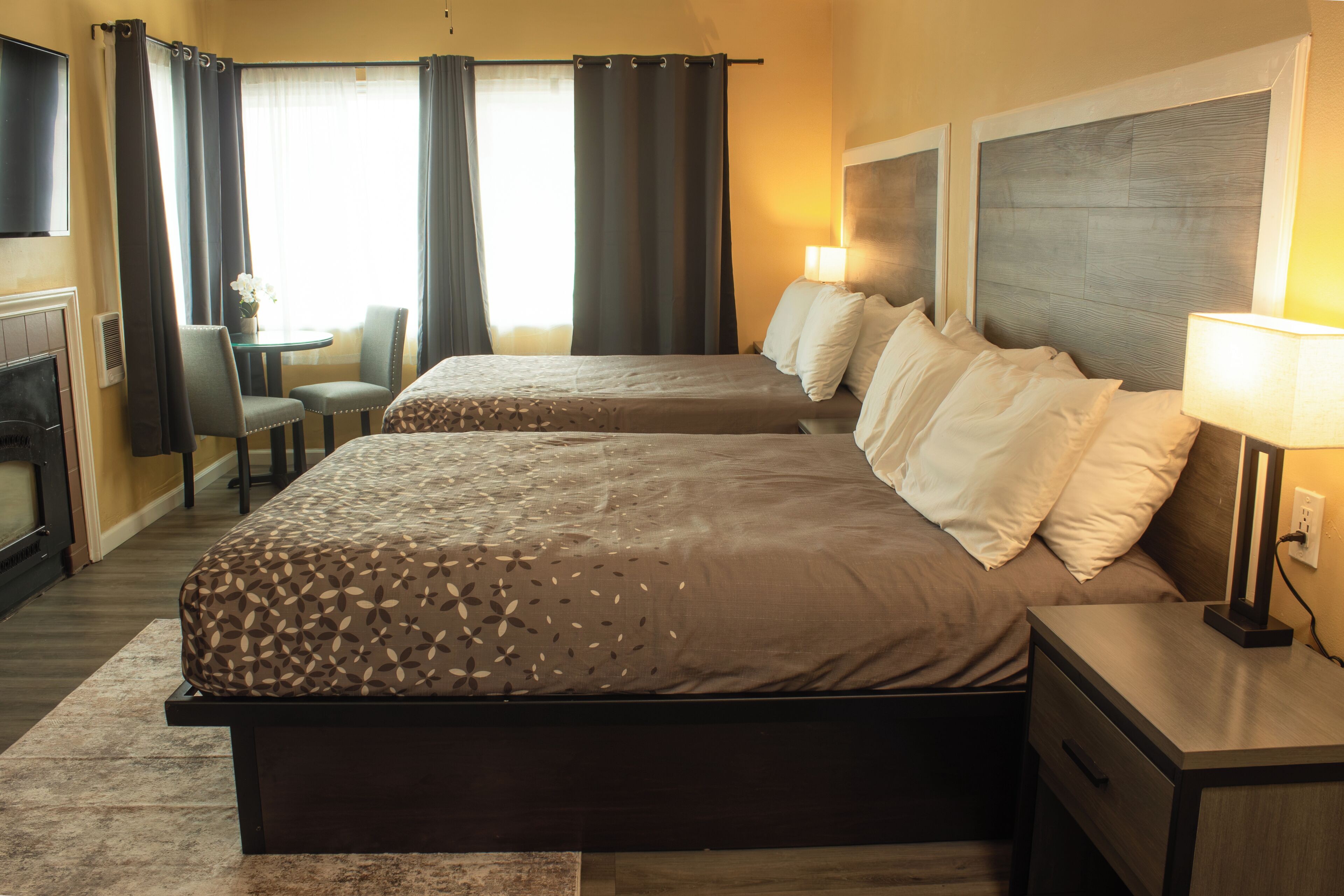 A hotel room with two beds, a desk, a chair, a lamp, and a fireplace.
