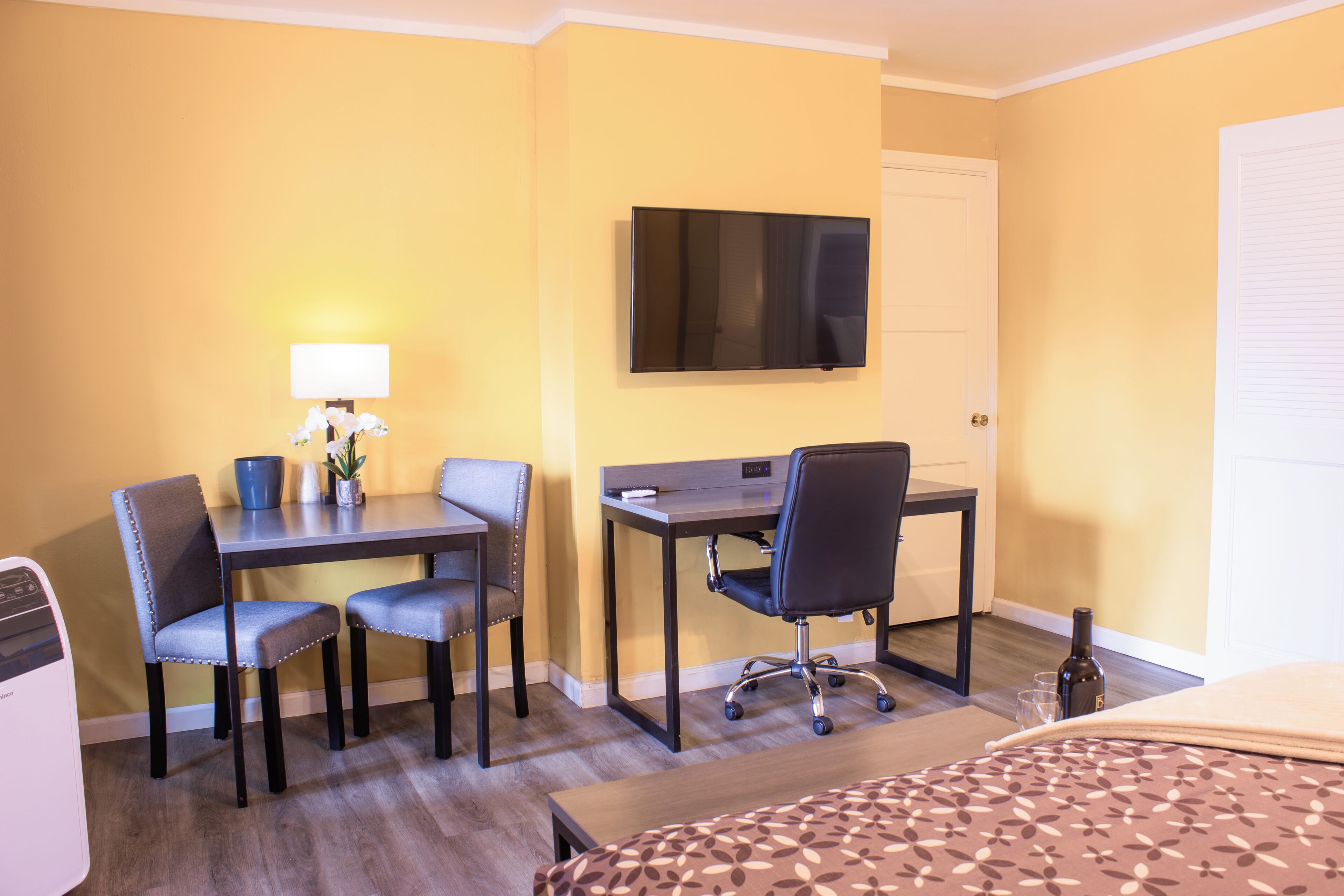 Habitación de hotel con escritorio, dos sillas, televisor, cama y una mesita con una botella y vasos.