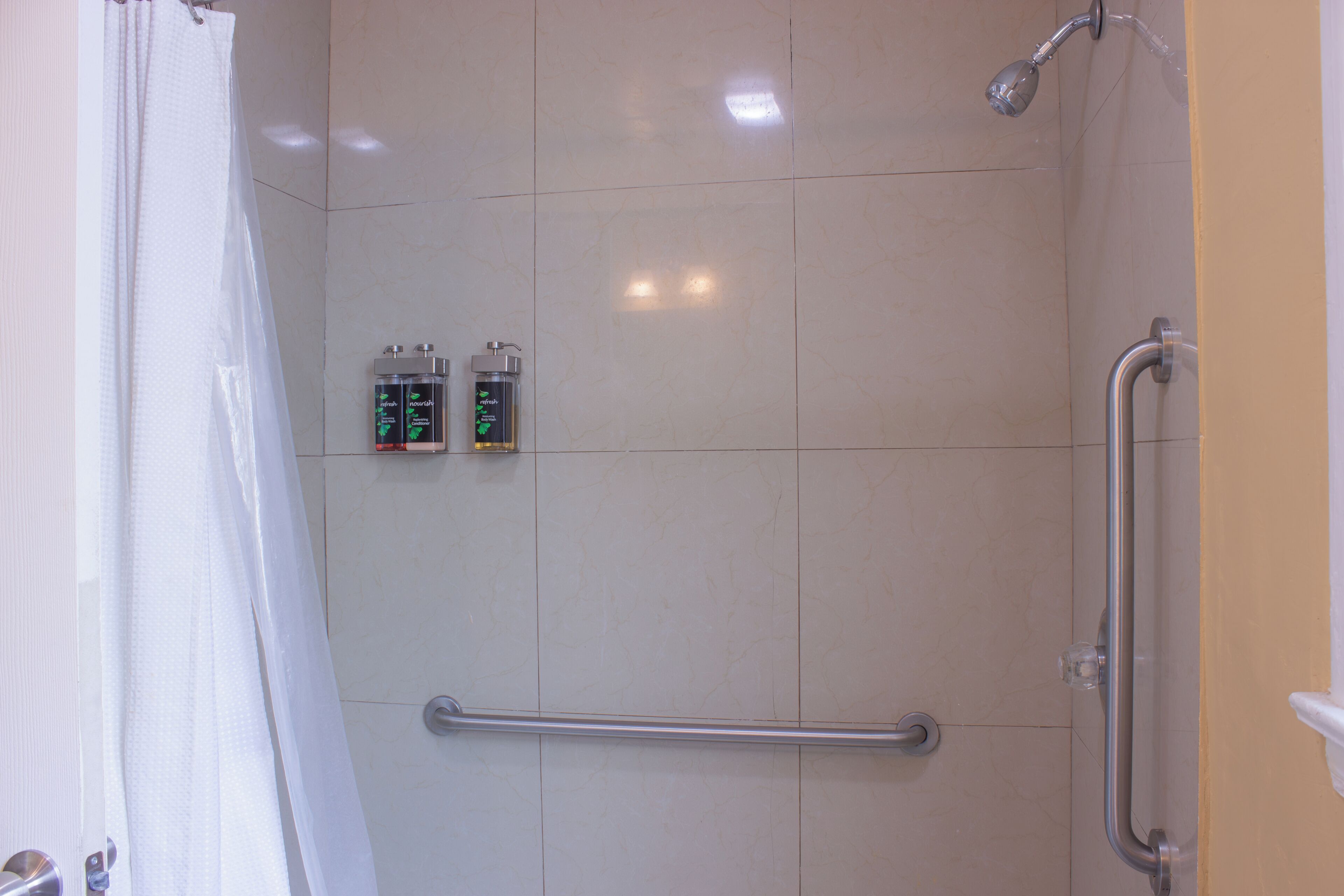 A shower area with a grab bar, a showerhead, and two bottles of body wash.