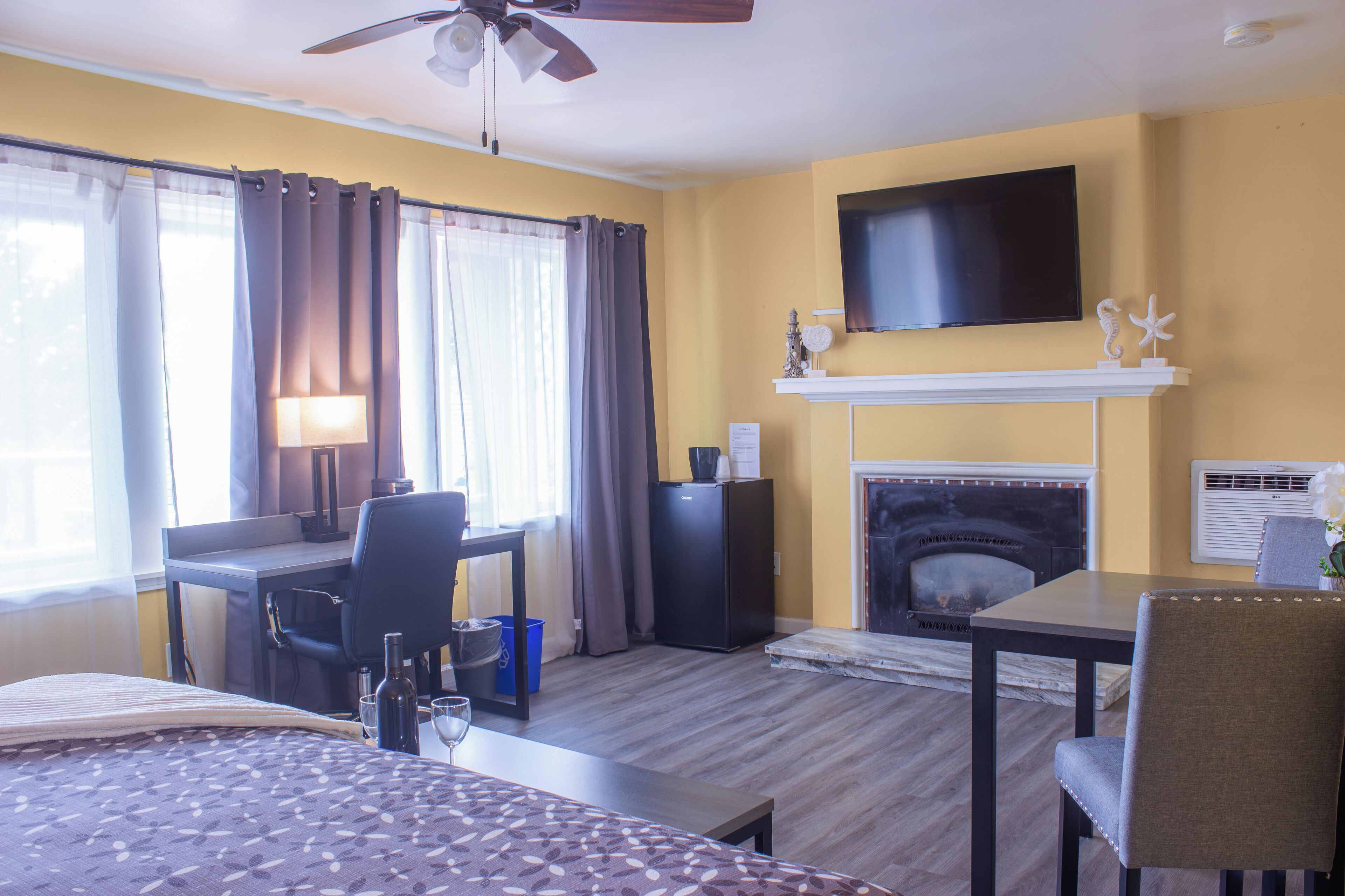 Habitación de hotel con cama, escritorio, silla, televisión, chimenea y ventilador de techo.