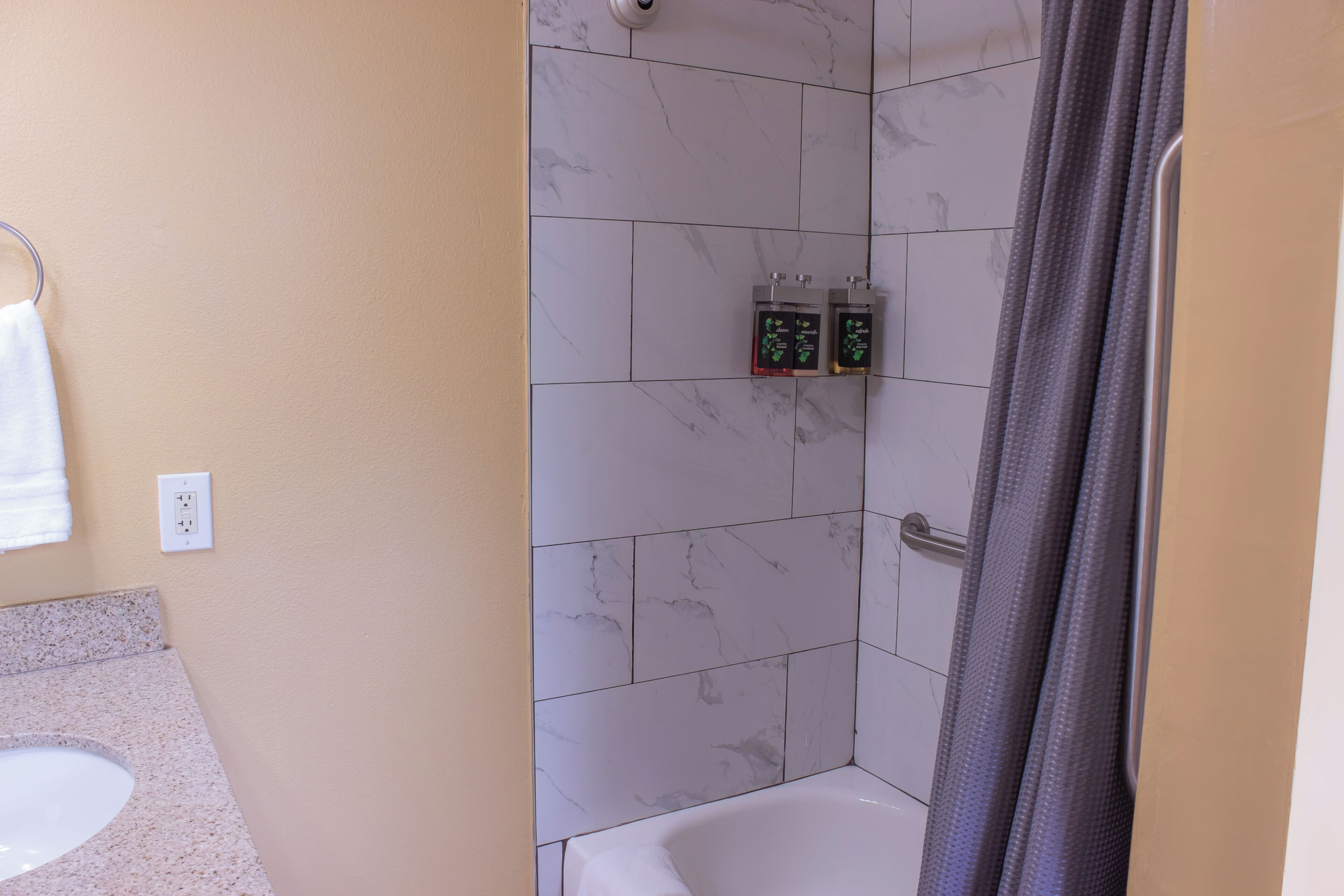 A bathroom with a white bathtub, a shower, and a toilet. There are two soap dispensers on the wall.