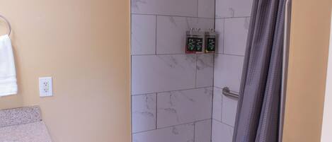 A bathroom with a white bathtub, a shower, and a toilet. There are two soap dispensers on the wall.