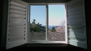 A window with white shutters, offering a view of a brick roof and trees.