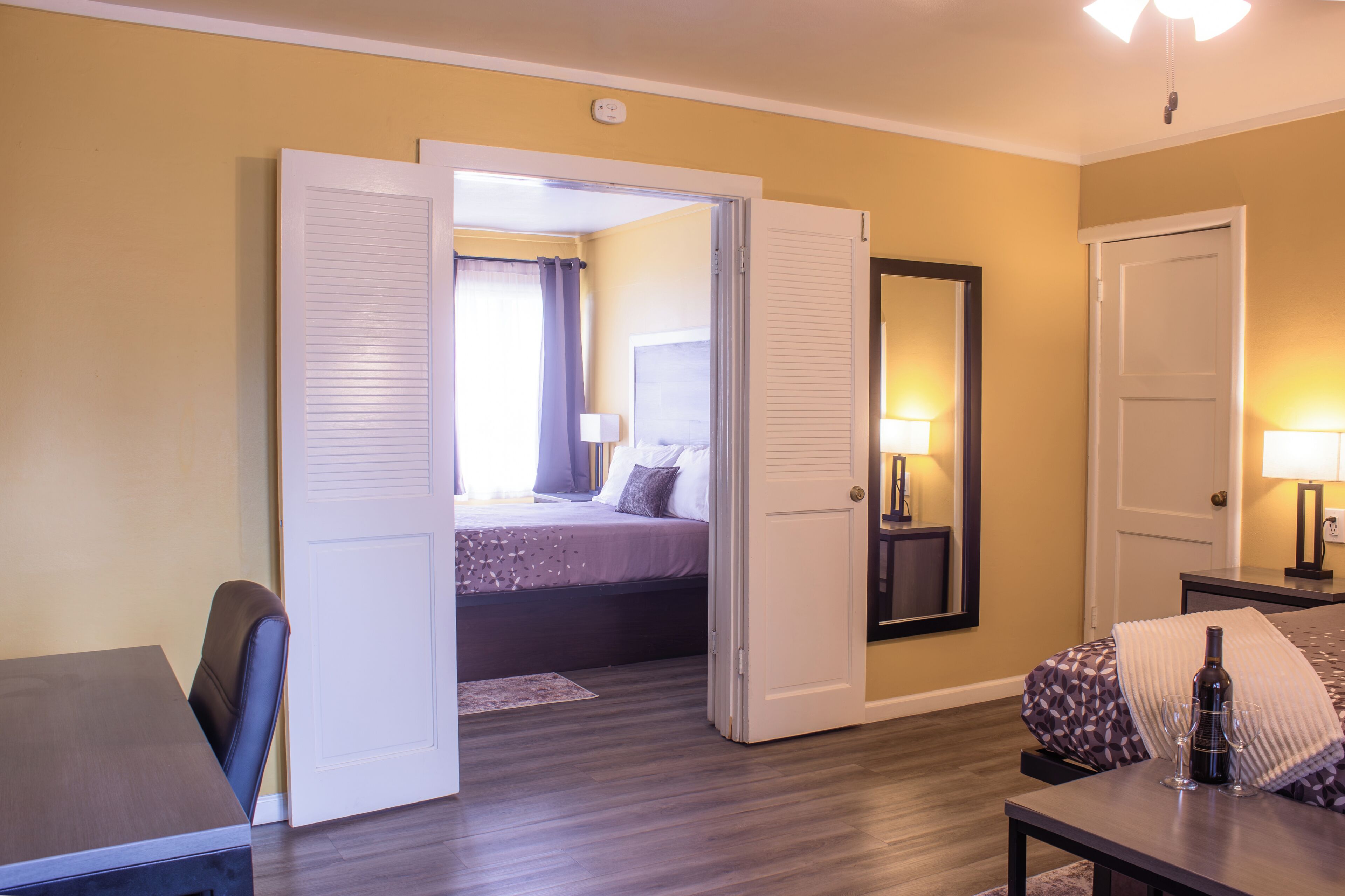 A hotel room with a bed, a desk, a chair, a table, and a mirror.