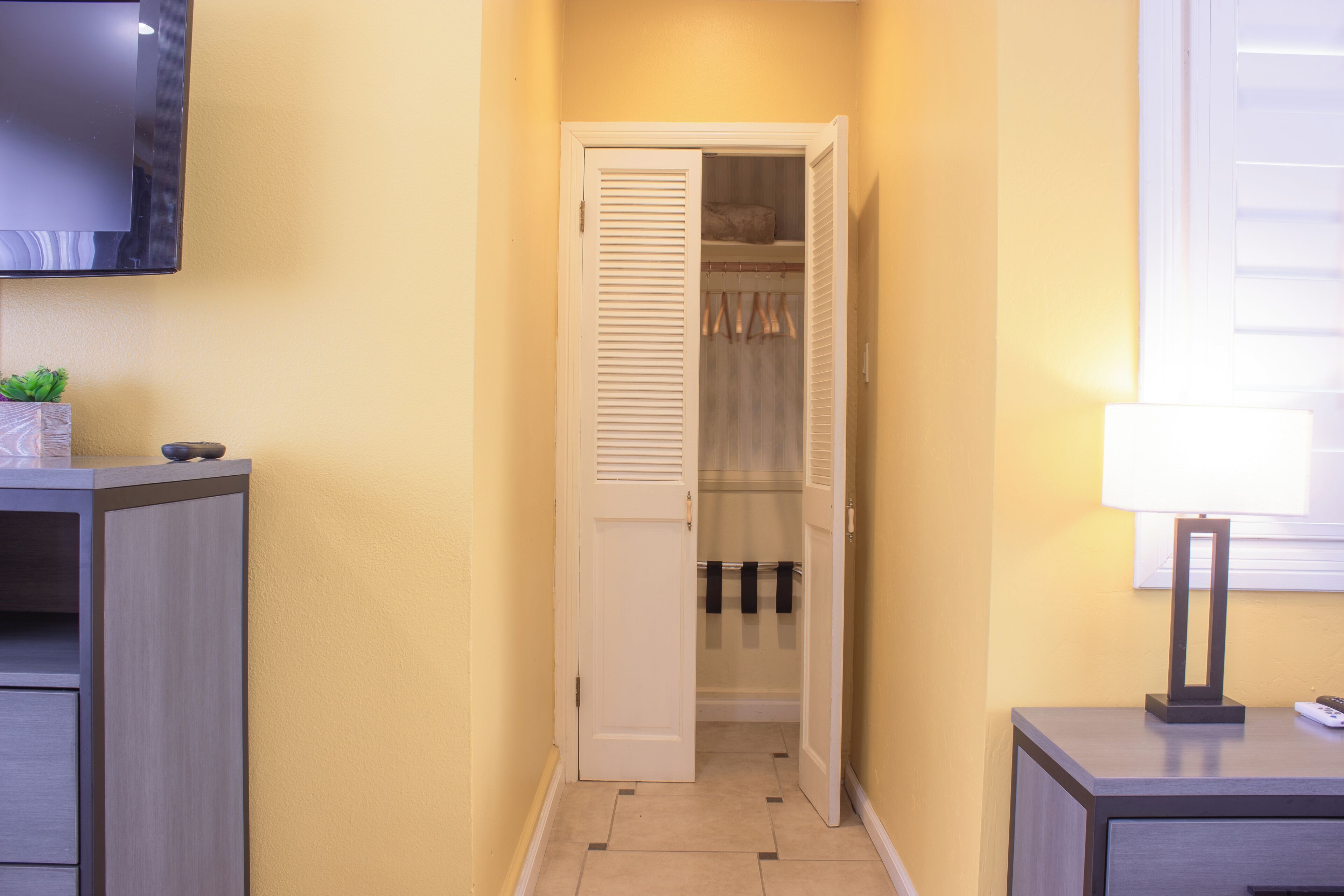 Un couloir avec une porte fermée, une petite table avec une lampe et un téléviseur fixé au mur.