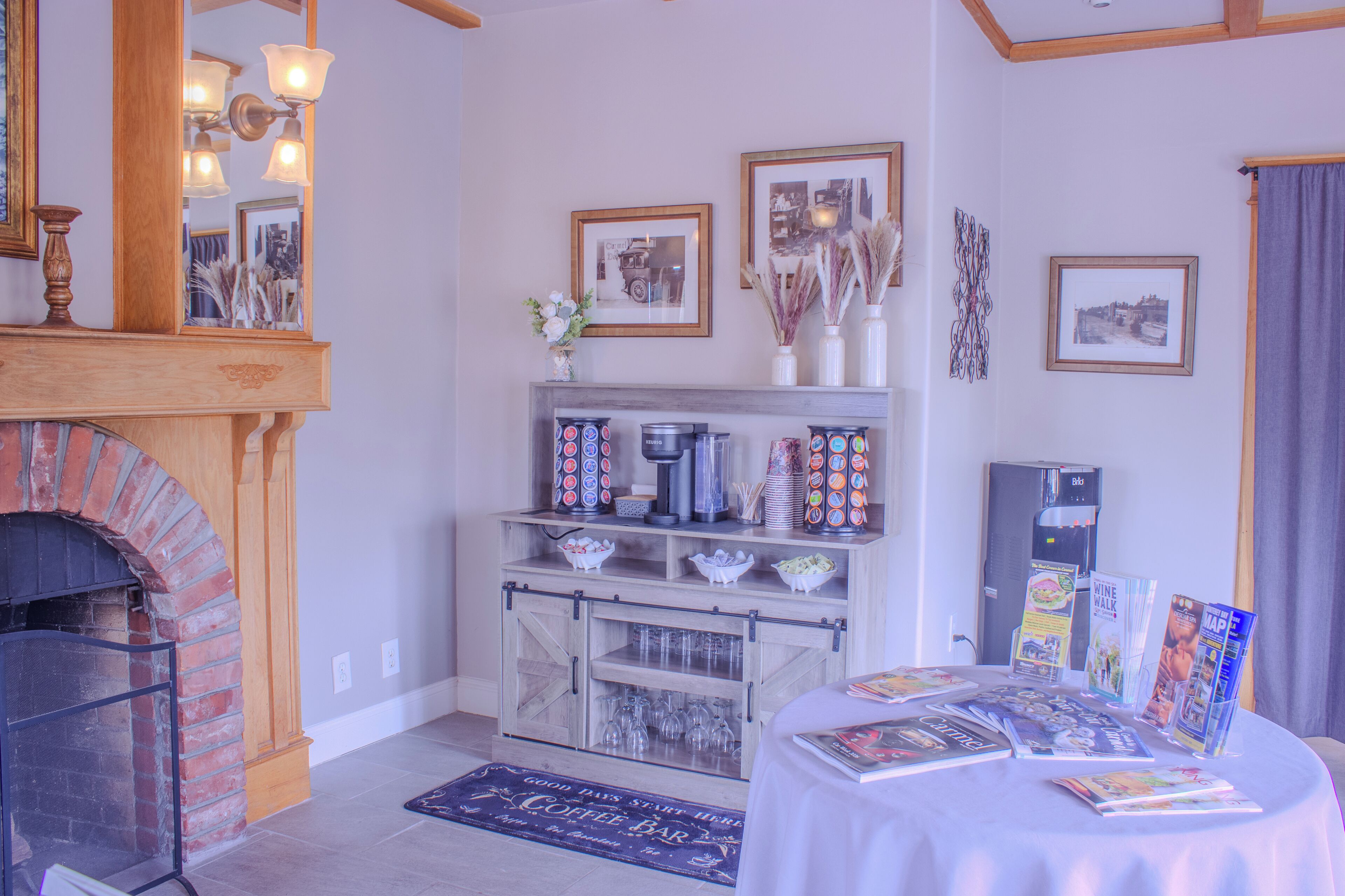 A cozy room with a fireplace, a coffee station, and various framed pictures on the walls.