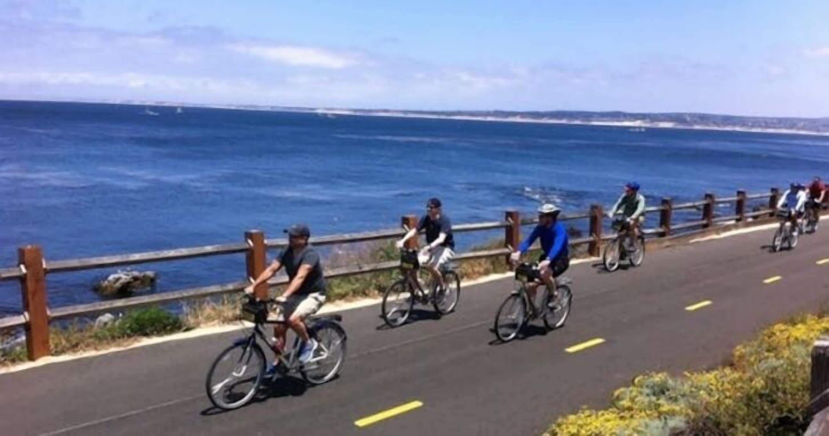 Una carretera costanera amb ciclistes, una tanca de fusta i l'oceà al fons.
